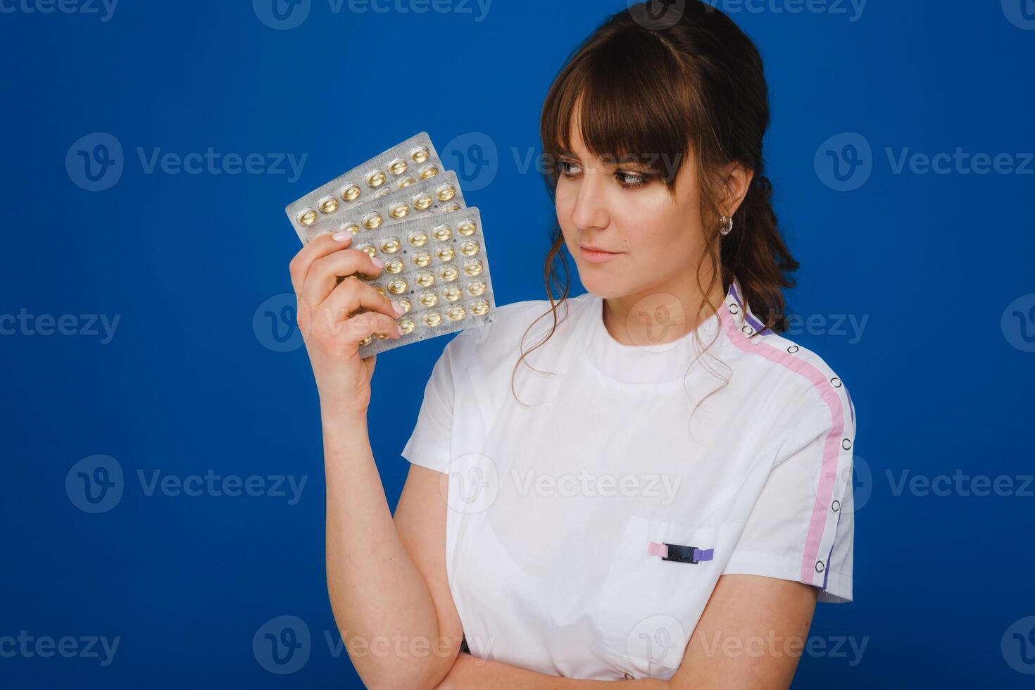 il concetto di Salute cura. un' giovane brunetta medico nel un' bianca cappotto su un' blu sfondo Spettacoli piatti con capsule per prendere. foto