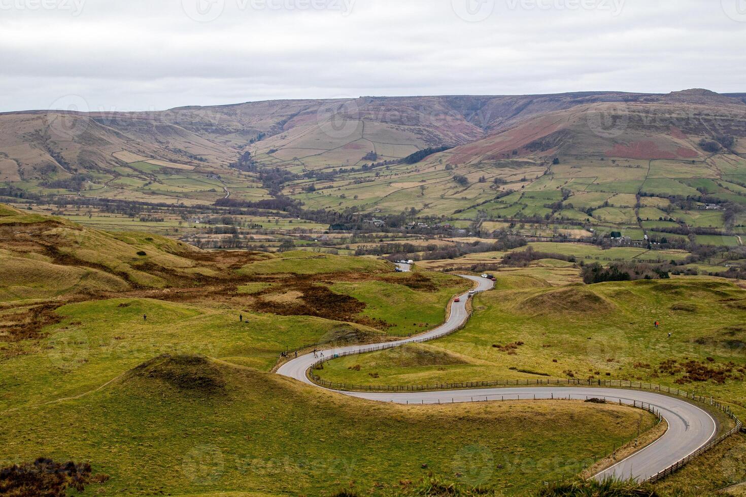 avvolgimento strada attraverso un' lussureggiante, verde valle con rotolamento colline sotto un' nuvoloso cielo nel picco quartiere, Inghilterra. foto