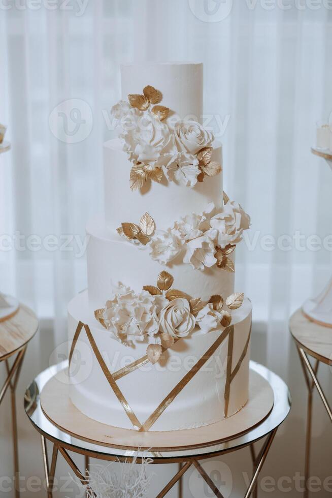 un' grande lussuoso multilivello nozze torta è decorato con fresco bianca rosa fiori nel il banchetto sala. nozze dolce sotto il sera luce. nozze arredamento. foto