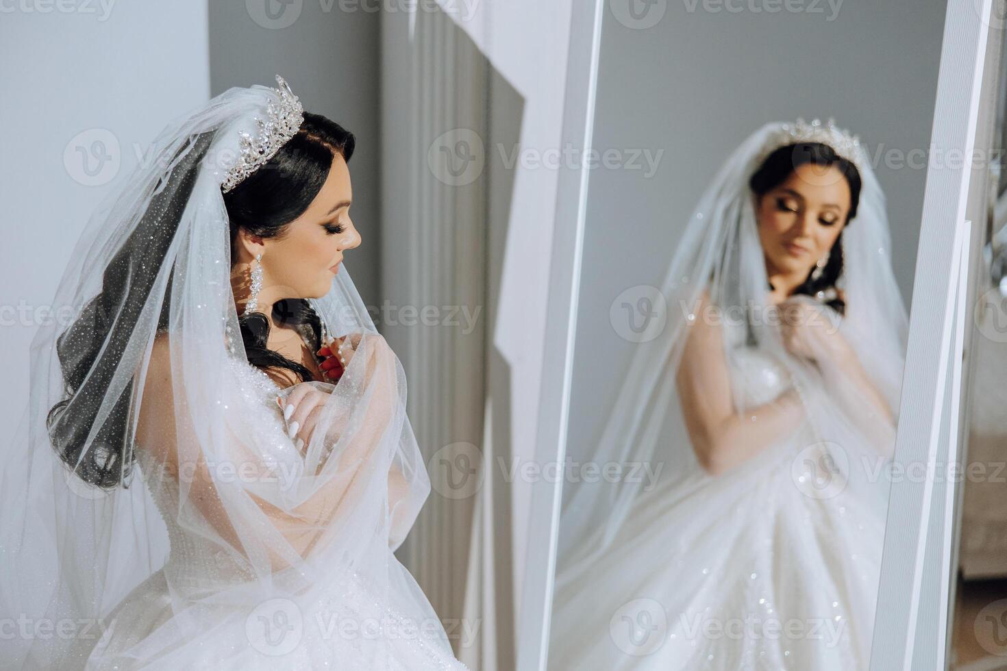 un' giovane europeo donna con buio capelli nel un' nozze vestito sta di un' specchio nel un' studio decorato con fiori. giovane bellissimo sposa. foto