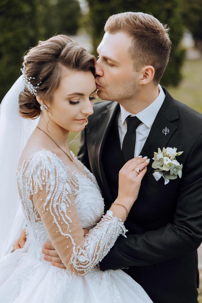 un' giovane sposa e sposo teneramente abbraccio nel il raggi di il autunno sole. tenero e bellissimo giovane ragazza sposa. un' uomo baci il suo Amati. contro il sfondo di un' bellissimo giardino foto