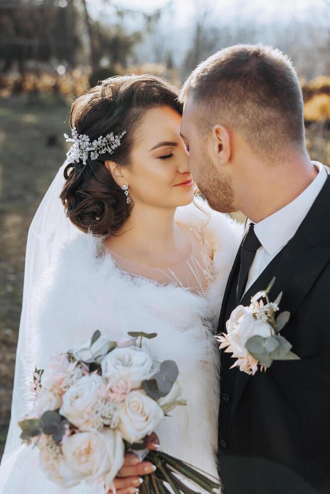 un' giovane sposa e sposo teneramente abbraccio nel il raggi di il autunno sole. tenero e bellissimo giovane ragazza sposa. un' uomo baci il suo Amati. contro il sfondo di un' bellissimo giardino foto