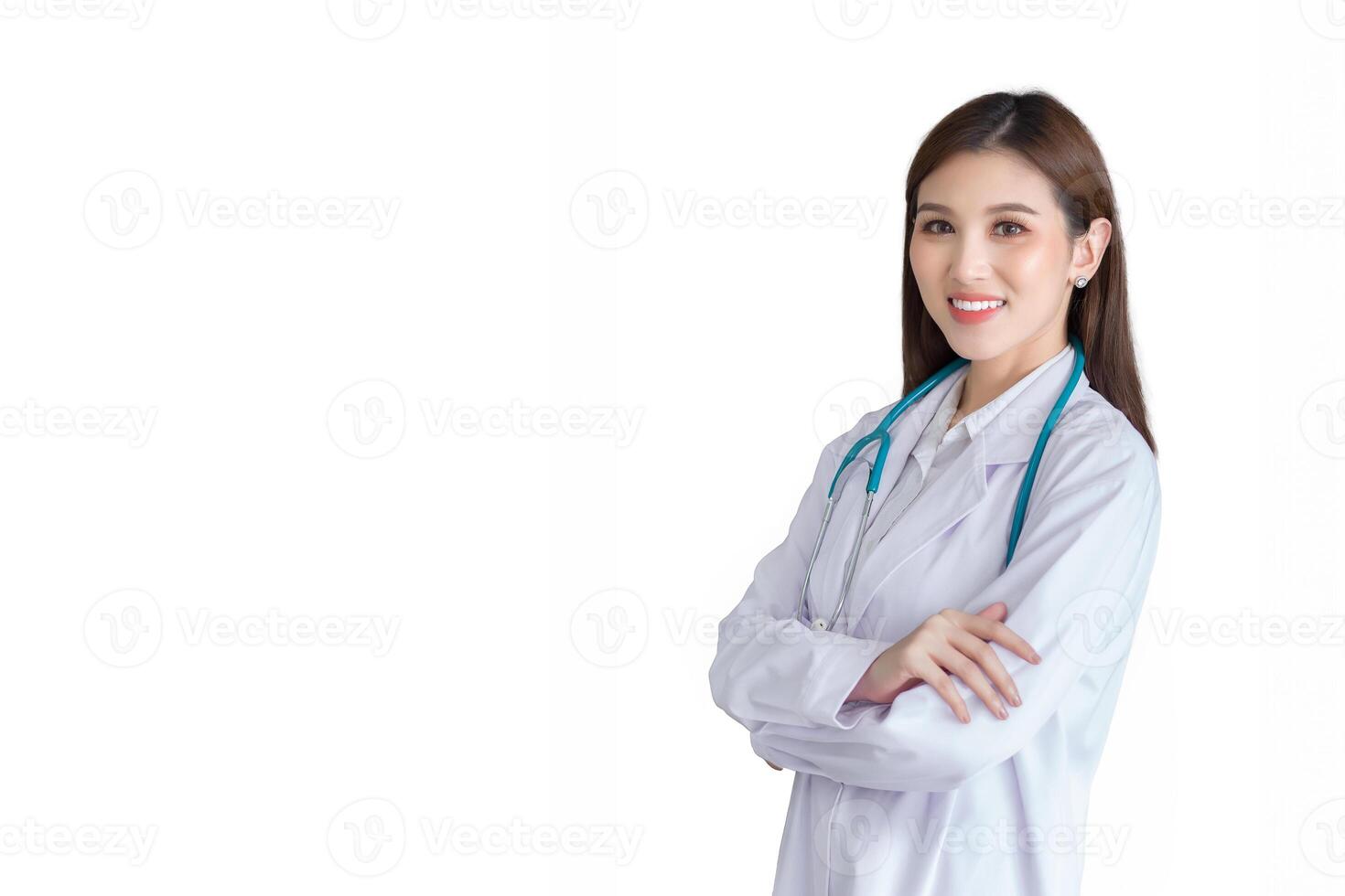 giovane asiatico professionale donna medico in piedi con fiducia con braccia attraversato indossare bianca accappatoio e stetoscopio a visita medica camera nel ospedale mentre isolato bianca sfondo. foto