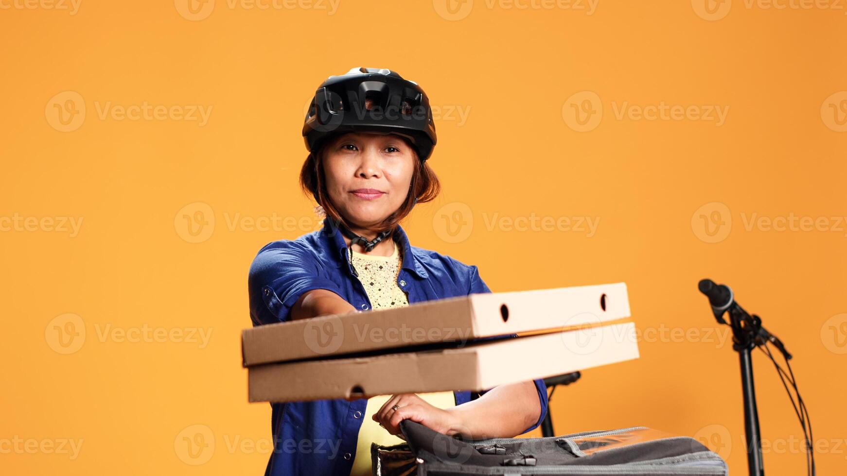 vicino su di Corriere donna isolato al di sopra di arancia studio sfondo portando Pizza per cliente. asiatico bicicletta ciclista consegna porta via cibo per cliente, assunzione pasto scatole su di termico Borsa foto