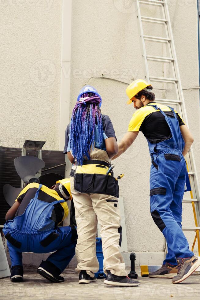 diverso squadra di competente meccanica Lavorando fuori, controllo per inceppato aria filtri ostacolante HVAC sistema flusso d'aria, causando riscaldamento sistema per opera Più forte e consumare Di Più energia foto