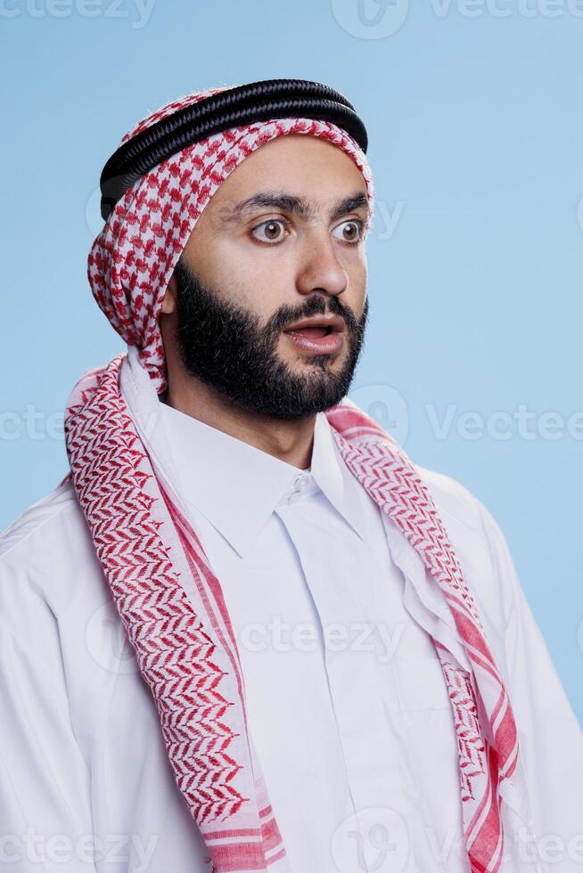 scioccato musulmano uomo vestito nel tradizionale foulard guardare lontano con largo occhi e Aperto bocca. persona indossare arabo ghutra e thobe Abiti mentre in posa con sorpreso viso espressione foto