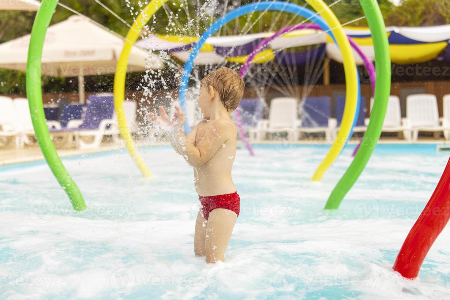 un' bambino sta sotto Fontana avendo divertimento con acqua spruzzi nel il piscina foto