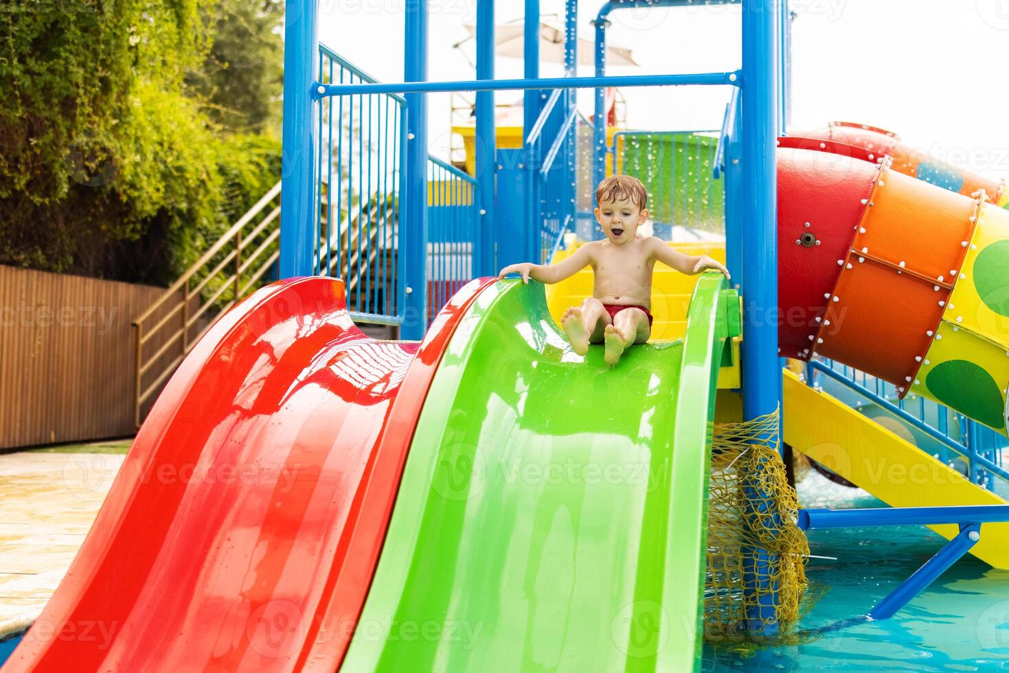 poco ragazzo giocando su acqua diapositiva nel all'aperto piscina su un' caldo estate giorno foto