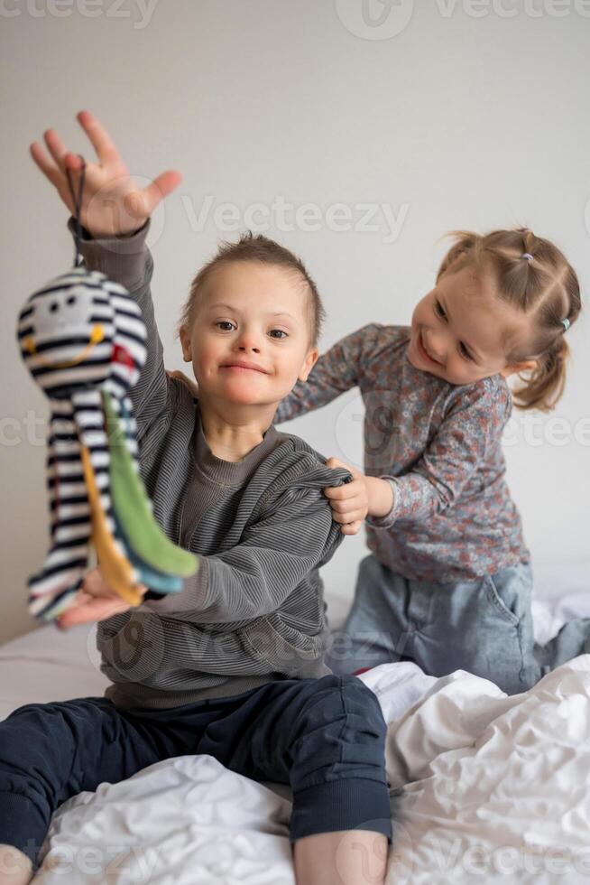 piccolo ragazzo con giù sindrome giochi con il suo minore sorella su il letto nel casa Camera da letto. alto qualità foto