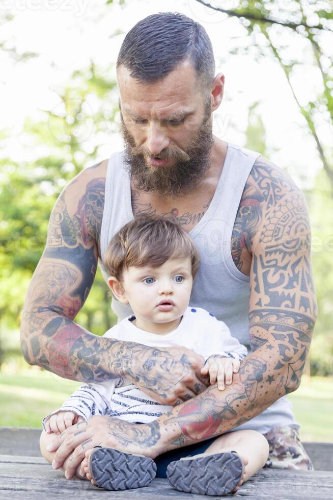 tatuato padre avere divertimento con il suo figlio nel il parco foto