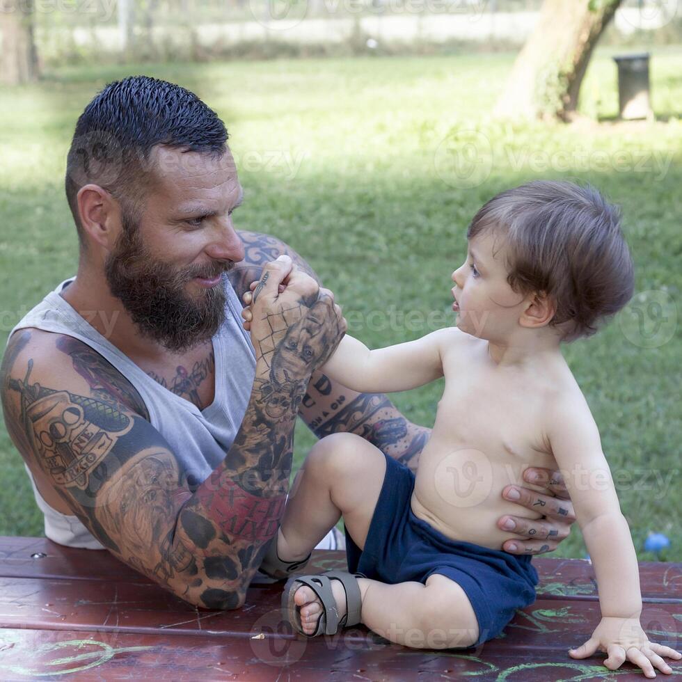 tatuato padre avere divertimento con il suo figlio nel il parco foto