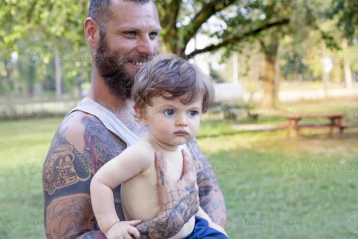tatuato padre avere divertimento con il suo figlio nel il parco foto
