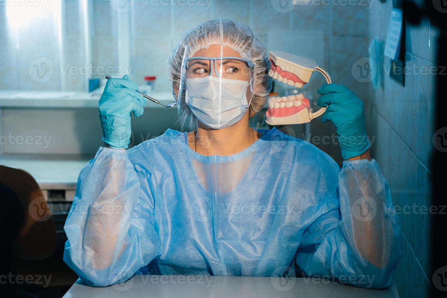 un' dentale medico indossare blu guanti e un' maschera detiene un' dentale modello di il superiore e inferiore fauci e un' dentale specchio foto