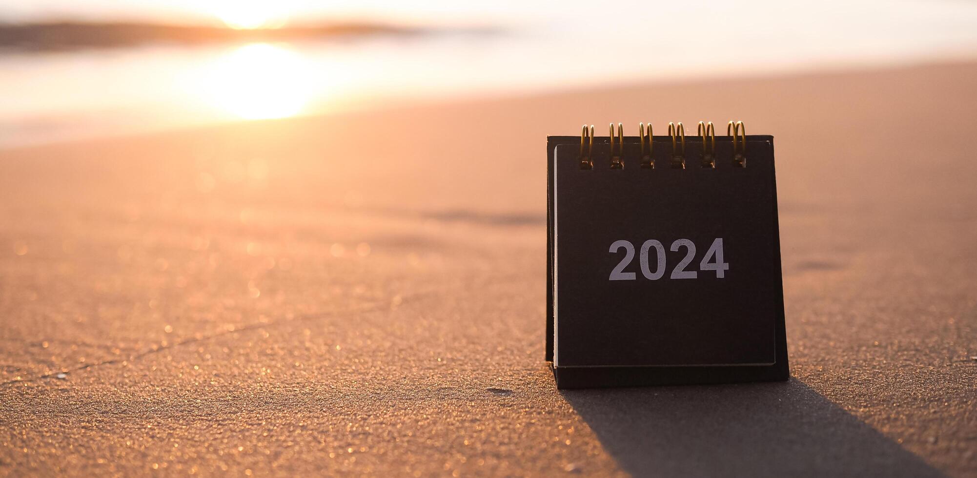 vicino su 2024 scrivania calendario su il spiaggia nel il tramonto volta. risoluzione, obiettivo, azione, pianificazione, e gestire per successo attività commerciale. foto