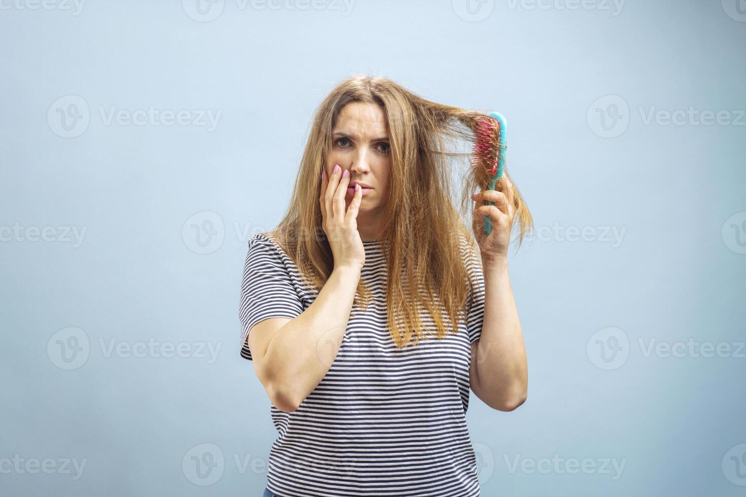 irritato giovane donna guardare con shock a sua danneggiato capelli su blu sfondo foto