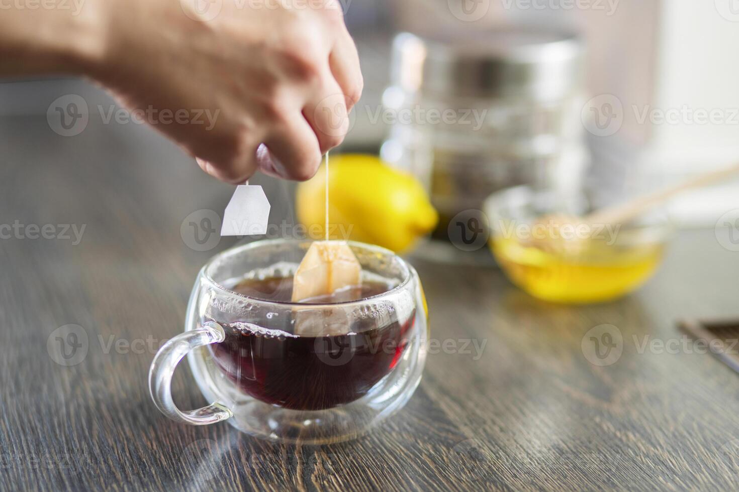 womans mano mette il tè Borsa nel il bicchiere tazza con caldo acqua foto