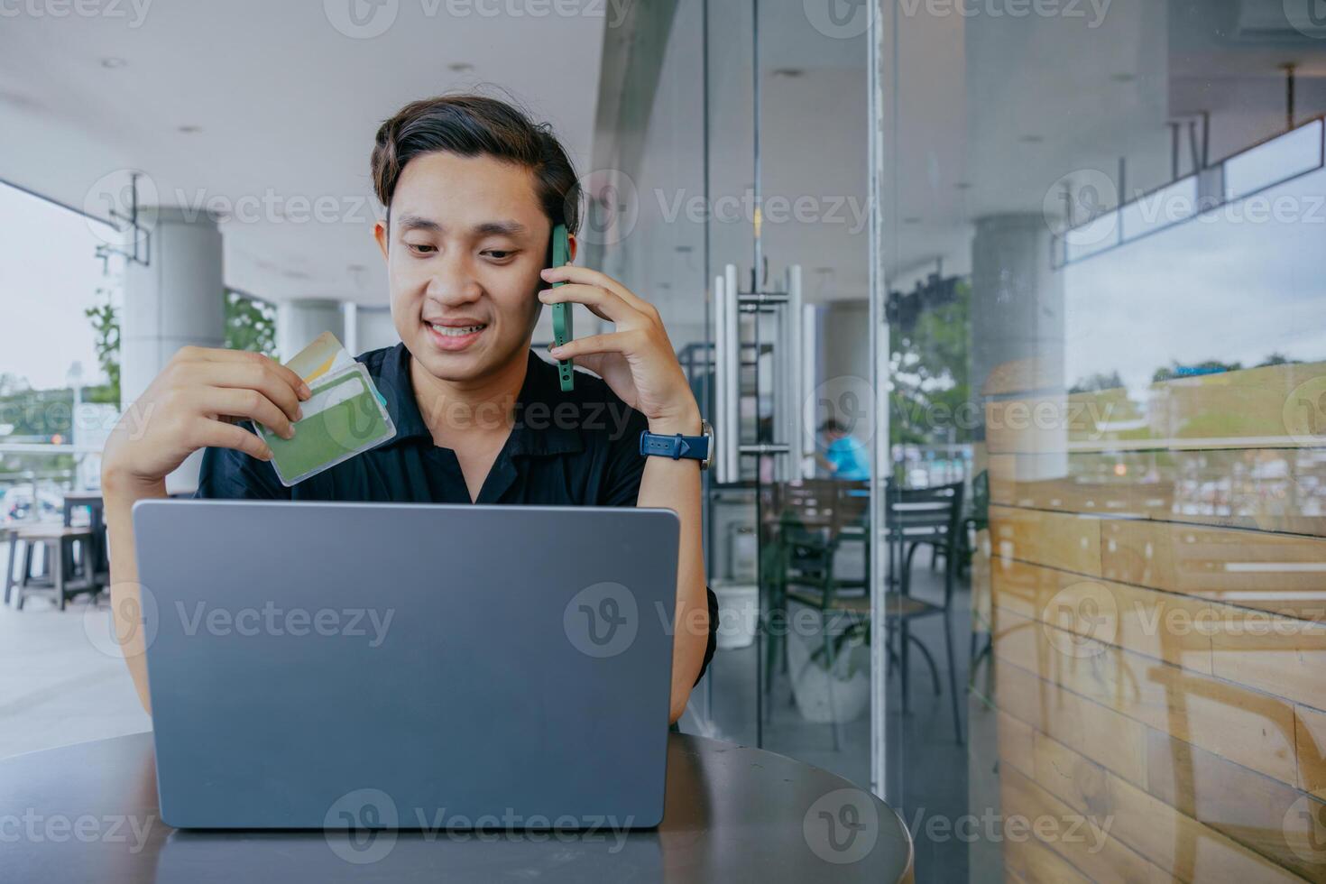 Internet acquisti. giovane asiatico uomo pagare per in linea Acquista, utilizzando credito carta, cellula Telefono e computer portatile, seduta a bar. foto