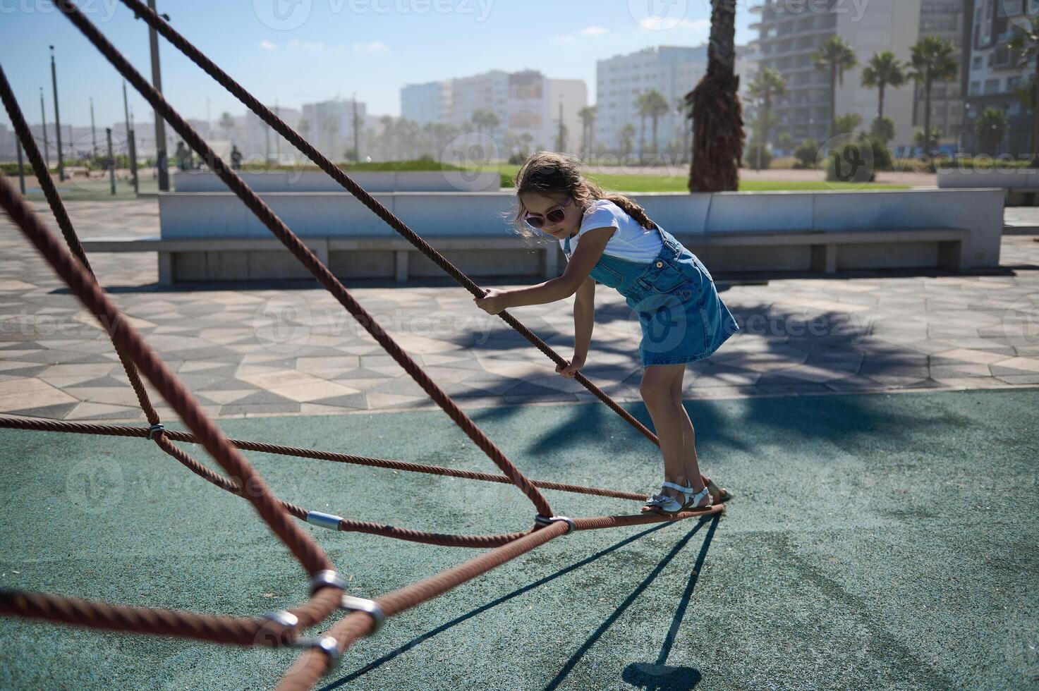 poco bambino ragazza la spesa attivo tempo arrampicata su il ragnatela nel il città terreno di gioco. bambino nel divertimento parco foto