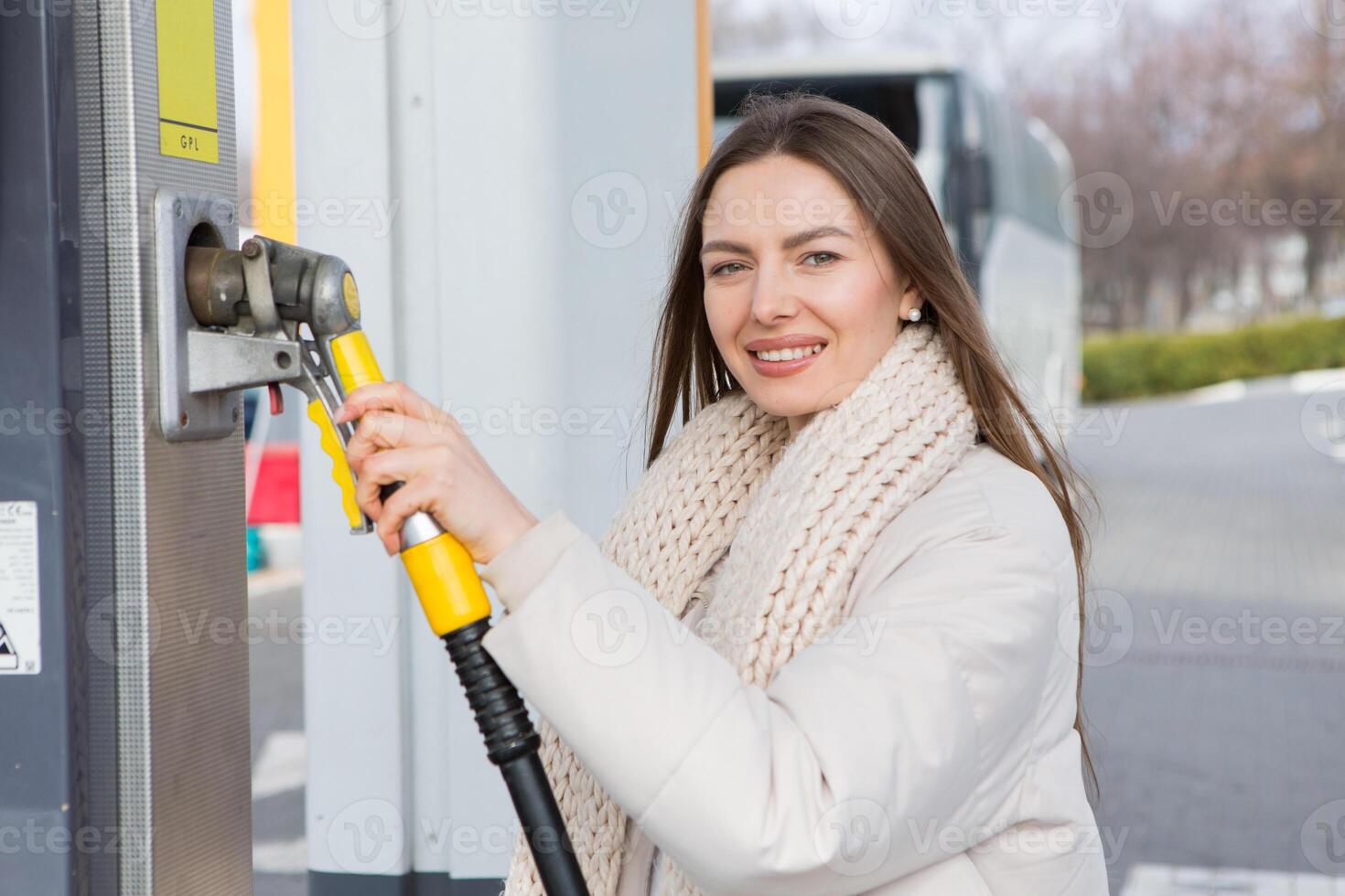 giovane donna Tenere un' carburante ugello nel sua mano mentre rifornimento carburante auto a gas stazione. un' fermare per rifornimento carburante a il gas stazione. fare il pieno il auto con gas. foto
