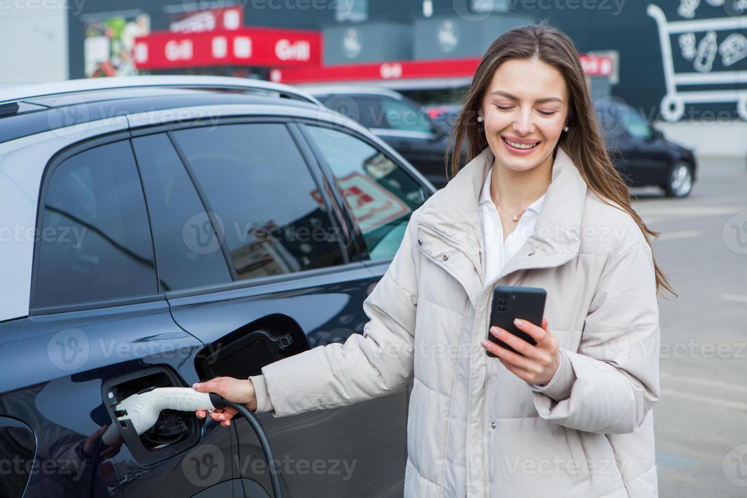 giovane donna ricarica sua elettrico auto a un' ricarica stazione nel il città. eco carburante concetto. il concetto di l'ambiente amichevole trasporto. ricarica batteria a partire dal ricarica stazione. foto