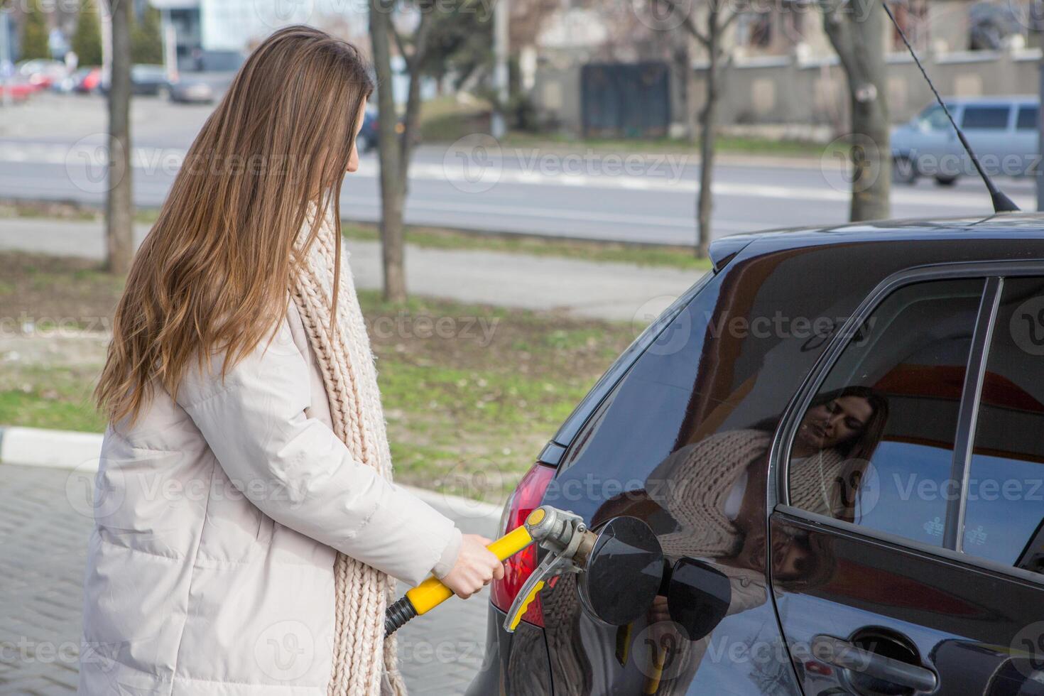 giovane donna Tenere un' carburante ugello nel sua mano mentre rifornimento carburante auto a gas stazione. un' fermare per rifornimento carburante a il gas stazione. fare il pieno il auto con gas. foto