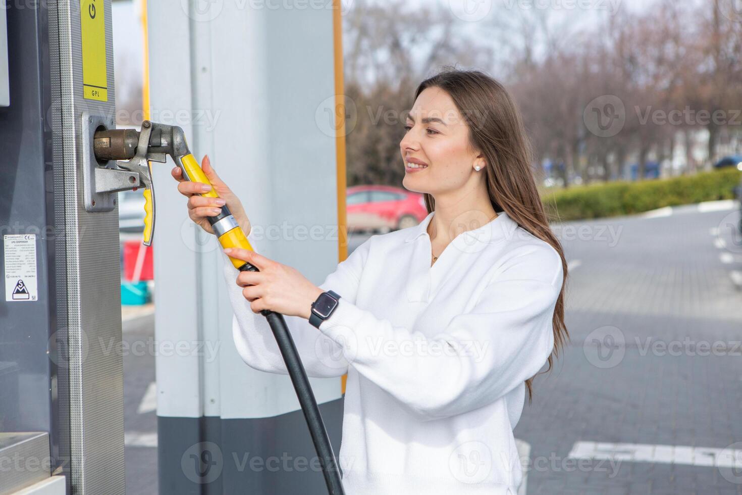 giovane donna Tenere un' carburante ugello nel sua mano mentre rifornimento carburante auto a gas stazione. un' fermare per rifornimento carburante a il gas stazione. fare il pieno il auto con gas. foto