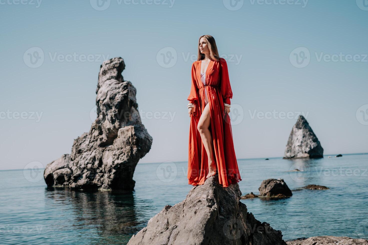 donna viaggio mare. giovane contento donna nel un' lungo rosso vestito in posa su un' spiaggia vicino il mare su sfondo di vulcanico rocce, piace nel Islanda, condivisione viaggio avventura viaggio foto