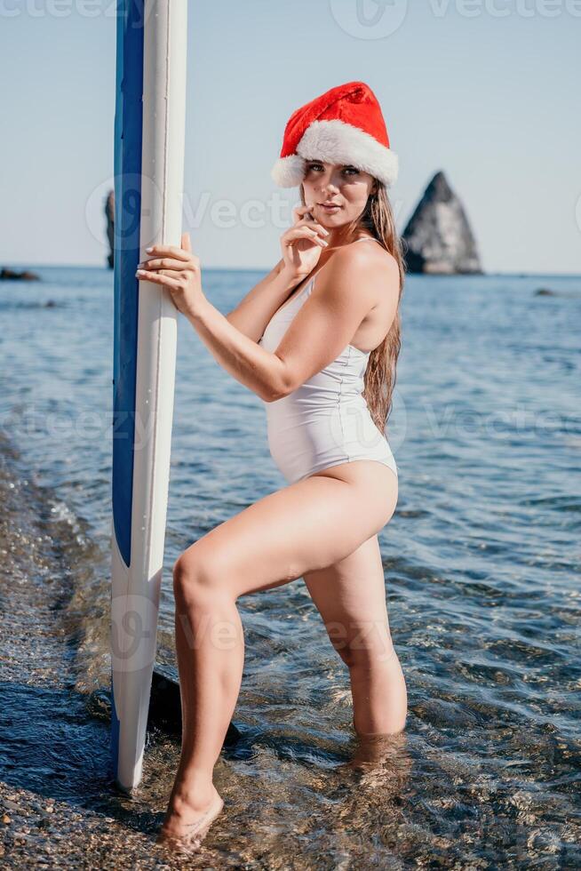 donna mare sup. vicino su ritratto di contento giovane caucasico donna con lungo capelli nel Santa cappello guardare a telecamera e sorridente. carino donna ritratto nel un' bianca bikini in posa su cenare tavola nel il mare foto