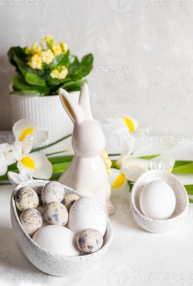 bianca vacanza decorazioni su Pasqua tavolo. uova nel ciotole con coniglietto orecchie, ceramica coniglietto, fiori. foto