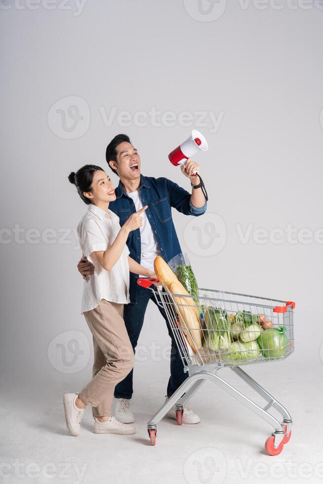 Immagine di asiatico coppia spingendo supermercato carrello mentre acquisti, isolato su bianca sfondo foto