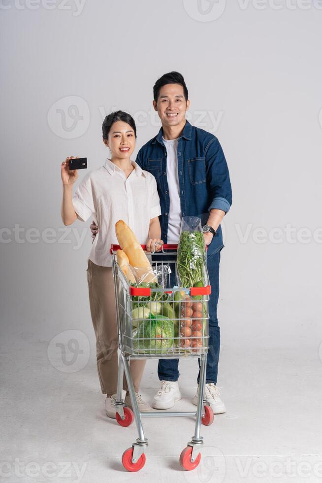 Immagine di asiatico coppia spingendo supermercato carrello mentre acquisti, isolato su bianca sfondo foto