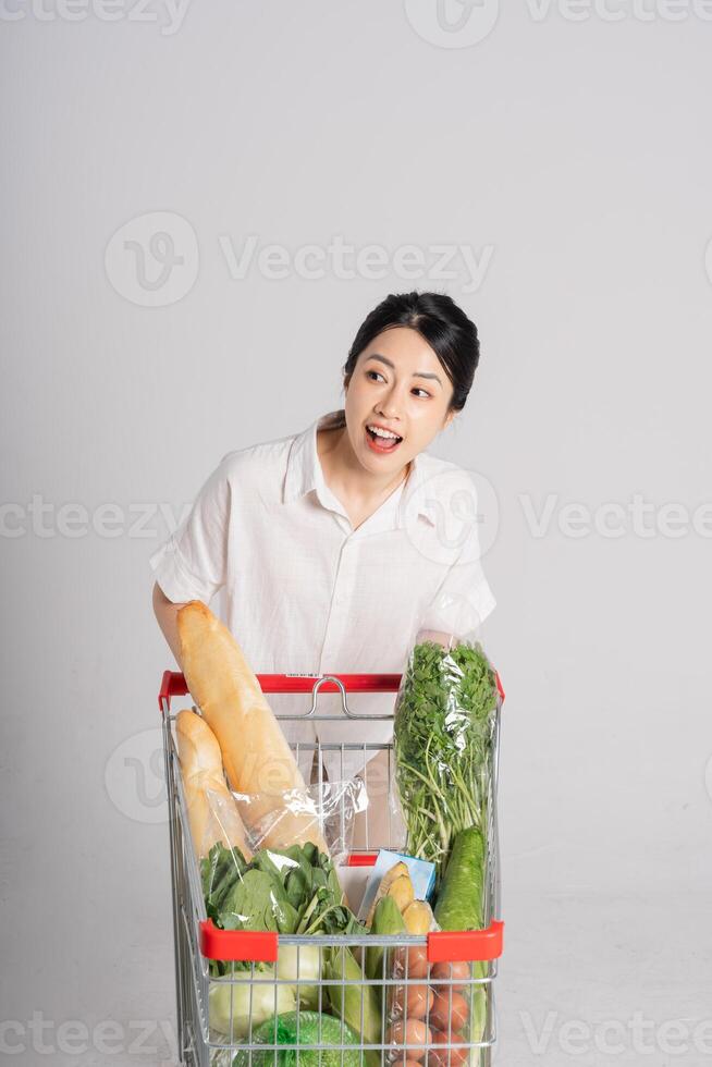 sorridente donna felicemente spingendo un' supermercato carrello, isolato su bianca sfondo foto