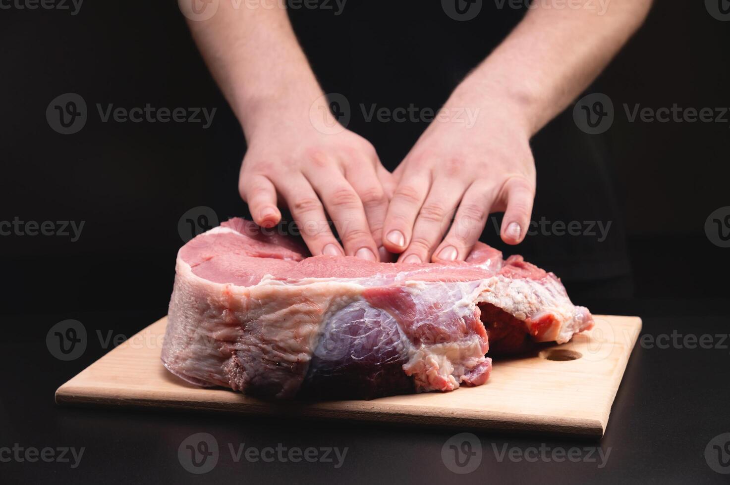 uomo massaggi un' fresco pezzo di Manzo con il suo mani su un' di legno taglio tavola. vicino su su nero sfondo foto