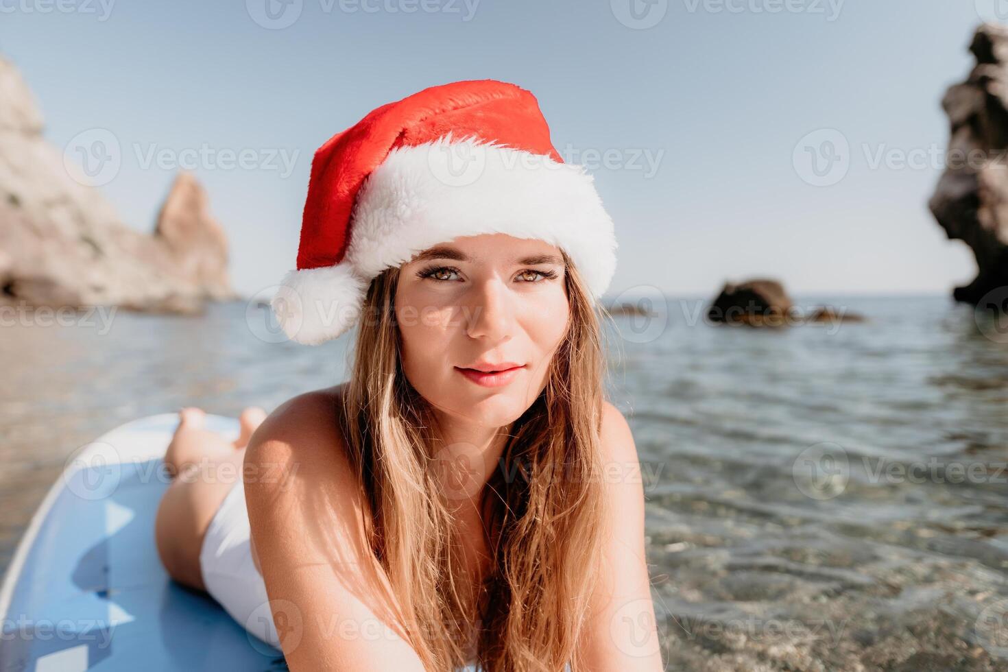 donna mare sup. vicino su ritratto di contento giovane caucasico donna con lungo capelli nel Santa cappello guardare a telecamera e sorridente. carino donna ritratto nel un' bianca bikini in posa su cenare tavola nel il mare foto