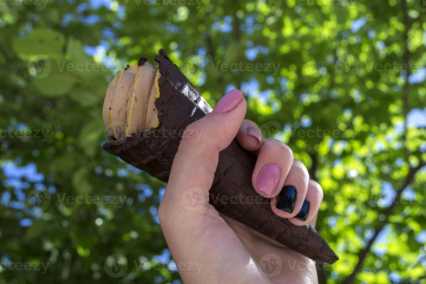 un ghiaccio crema cono nel femmina braccio contro un' verde albero sfondo foto