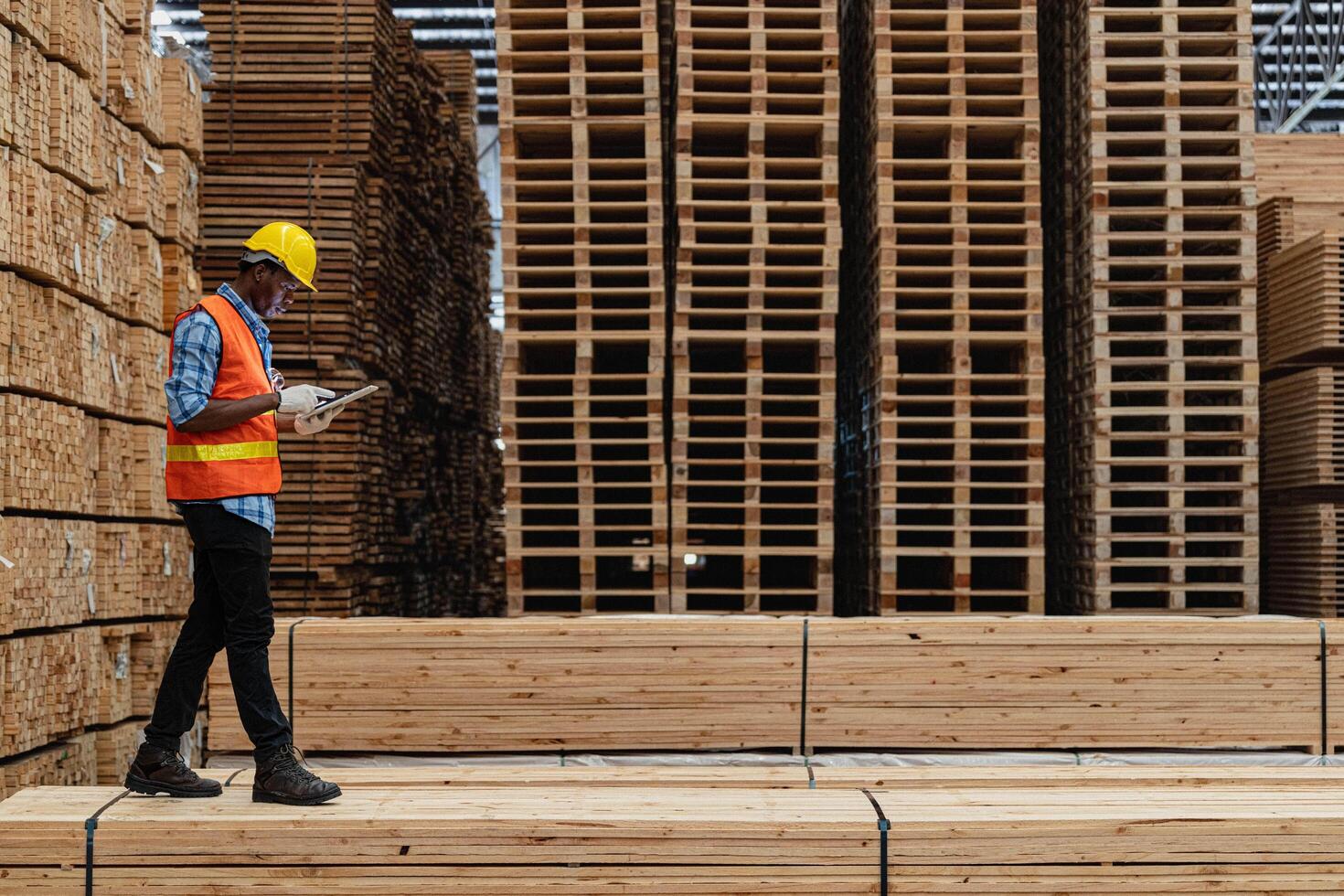 africano lavoratori uomo ingegneria a piedi e ispezionando con Lavorando suite vestito e mano guanto nel legname legna magazzino. concetto di inteligente industria lavoratore operativo. legna fabbriche produrre legna palato. foto