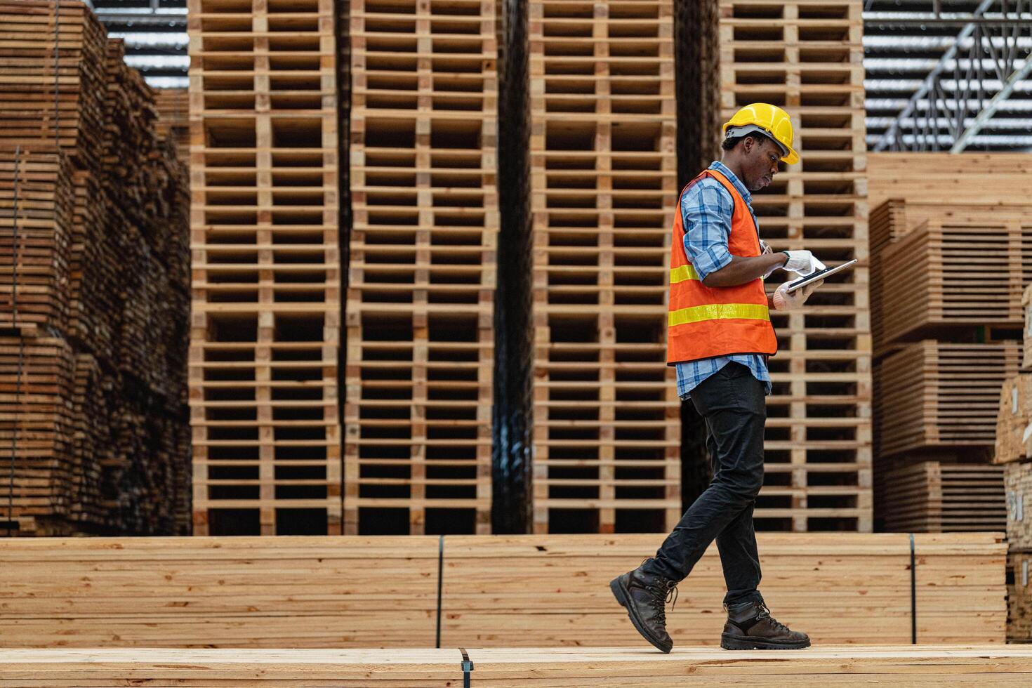 africano lavoratori uomo ingegneria a piedi e ispezionando con Lavorando suite vestito e mano guanto nel legname legna magazzino. concetto di inteligente industria lavoratore operativo. legna fabbriche produrre legna palato. foto