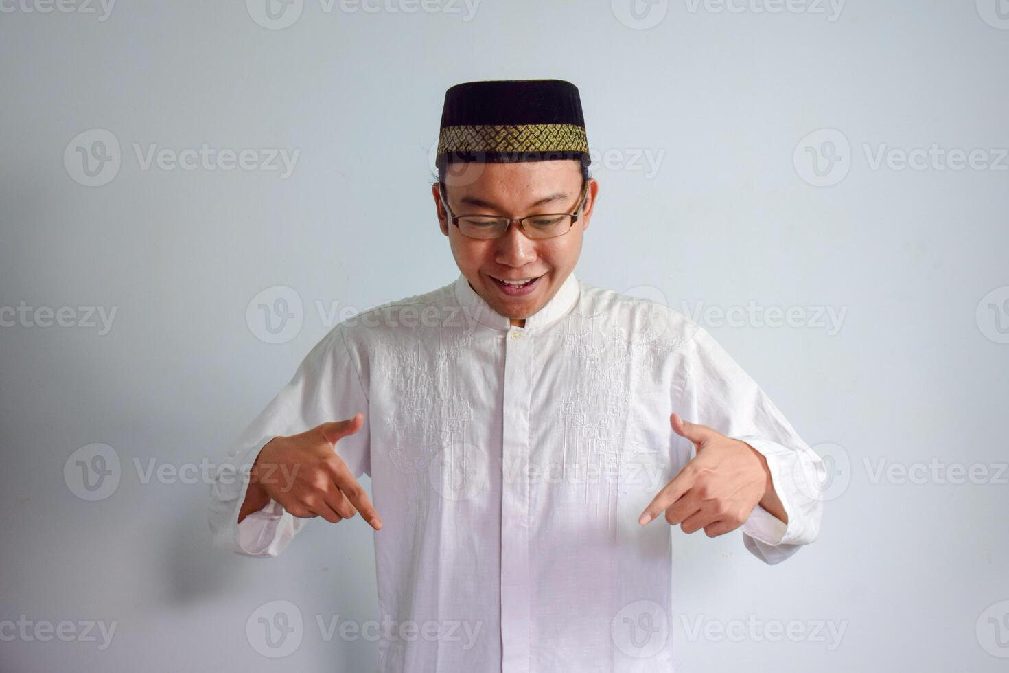 asiatico musulmano uomo indossare bicchieri e bianca stoffa puntamento giù posa per Ramadhan e eid al fitr. isolato bianca sfondo foto