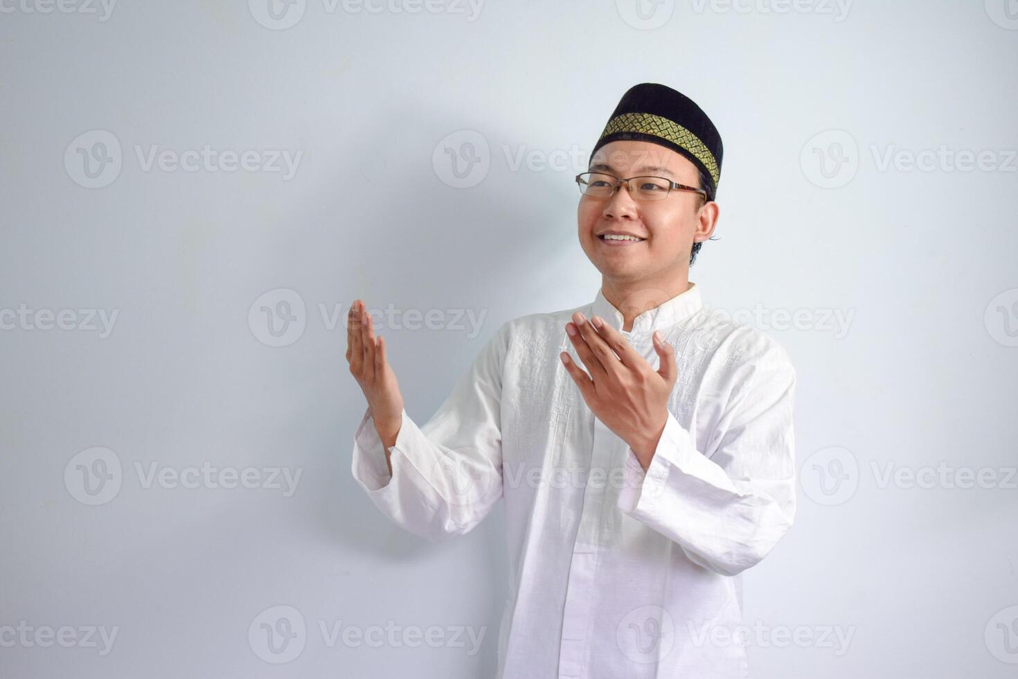 asiatico musulmano uomo indossare bicchieri e bianca stoffa fare preghiere mano posa per Ramadhan e eid al fitr. isolato bianca sfondo foto