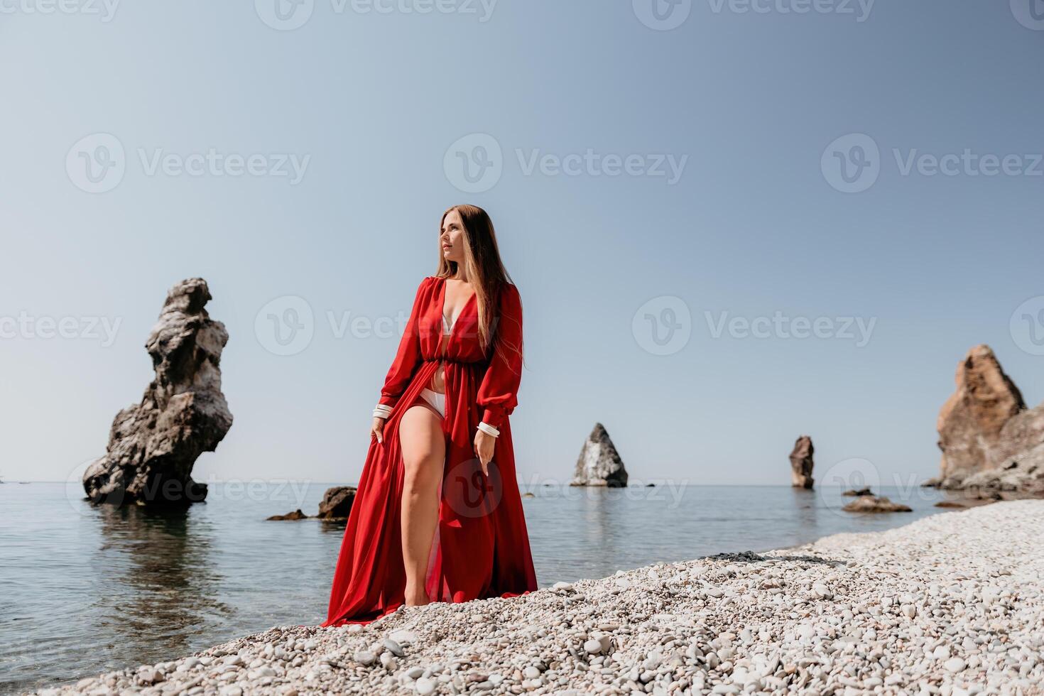 donna viaggio mare. contento turista nel rosso vestito godere assunzione immagine all'aperto per ricordi. donna viaggiatore in posa su il roccia a mare baia circondato di vulcanico montagne, condivisione viaggio avventura viaggio foto