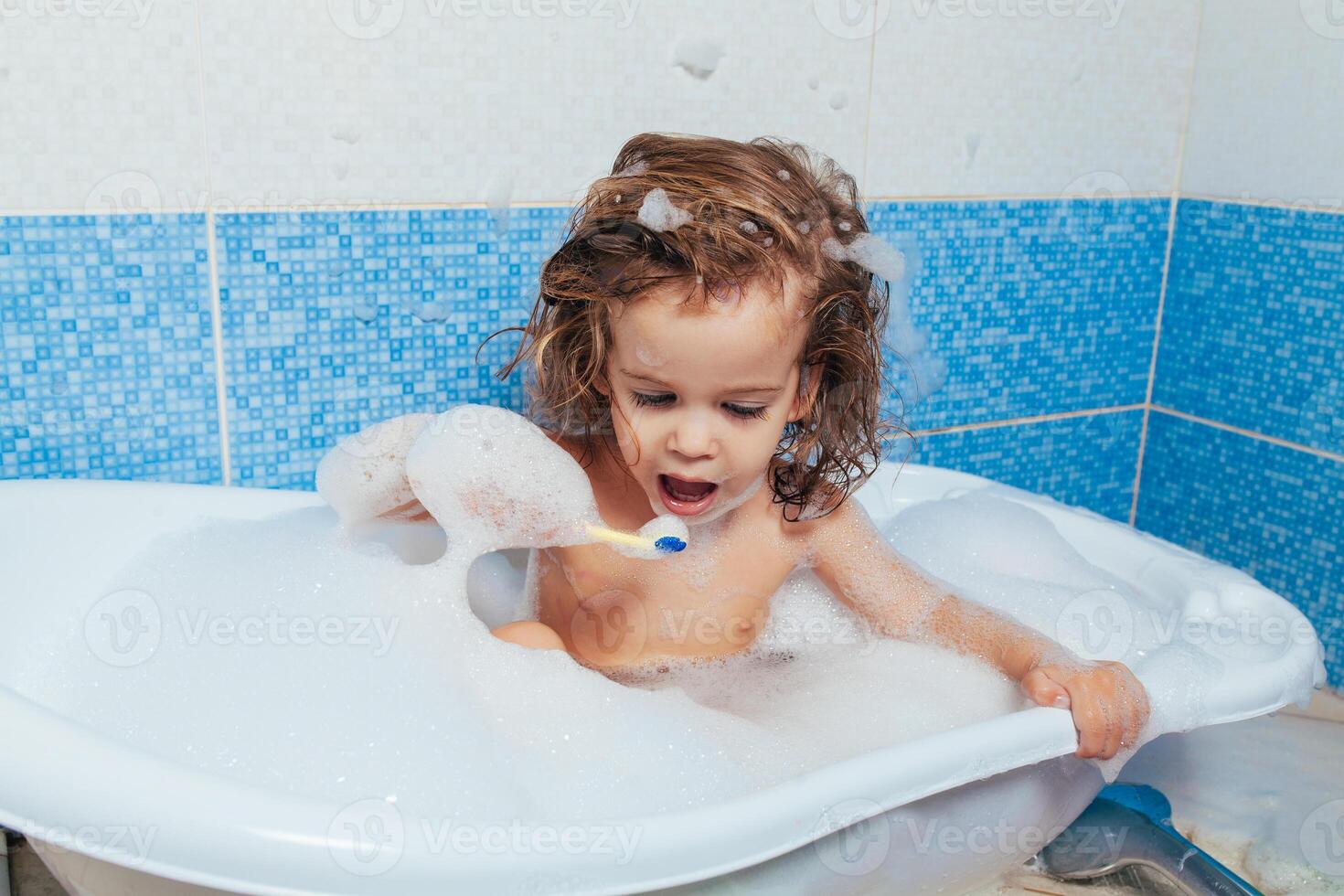 bellissimo giovane ragazza bagna nel il bagno e spazzole sua denti con un' spazzolino. quotidiano mattina routine. figli di igiene è divertimento foto