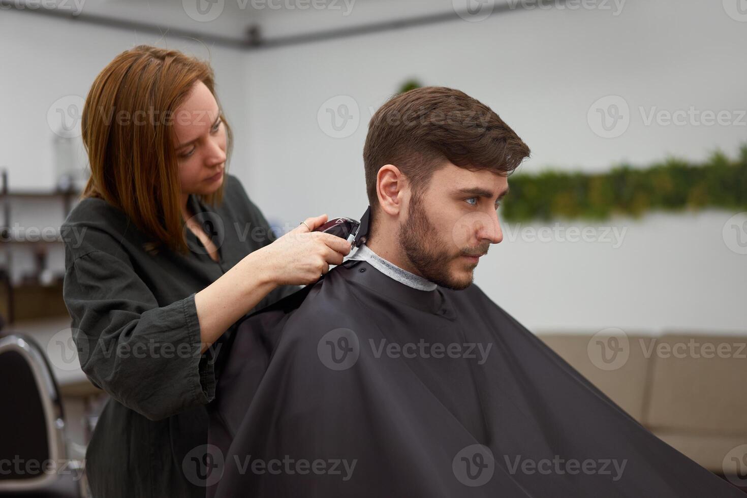 bello blu con gli occhi uomo seduta nel barbiere negozio. parrucchiere parrucchiere donna taglio il suo capelli. femmina barbiere. foto