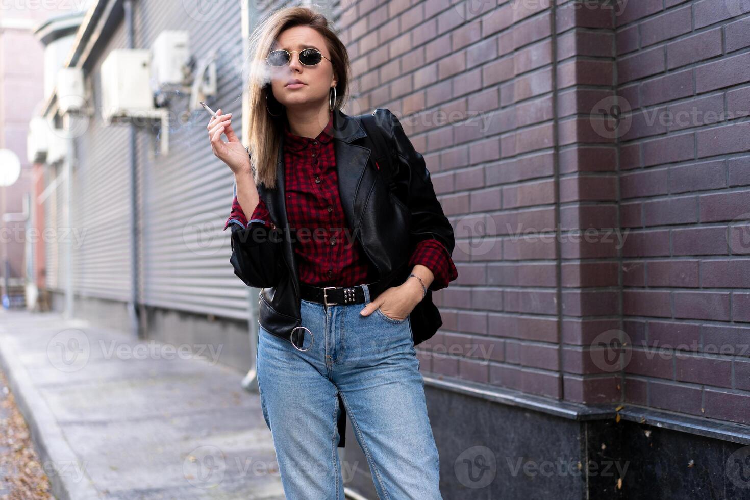 bellissimo giovane con stile vestito caucasico ragazza fuma sigaretta su il strada. foto