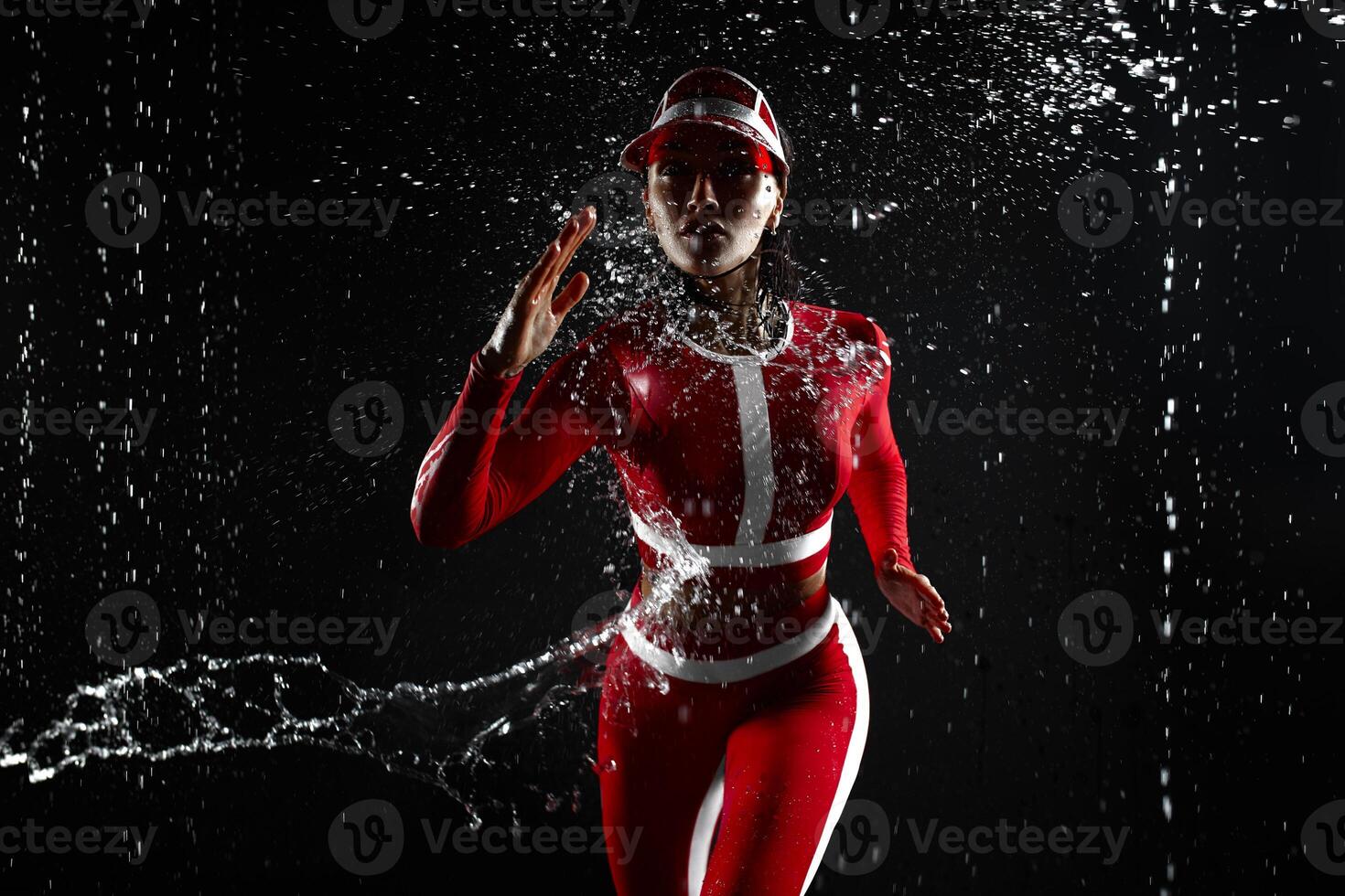 bellissimo giovane ragazza nel abbigliamento sportivo runing nel acqua studio. gocce di acqua diffusione di sua fitness corpo. il Perfetto figura su il sfondo di acqua schizzi. cattivo tempo metereologico per sport foto