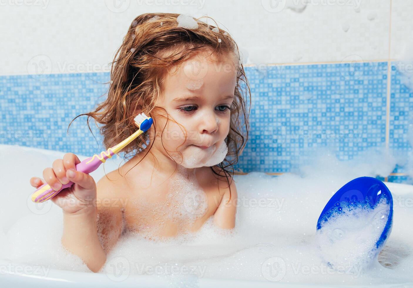 bellissimo giovane ragazza bagna nel il bagno e spazzole sua denti con un' spazzolino. quotidiano mattina routine. figli di igiene è divertimento foto