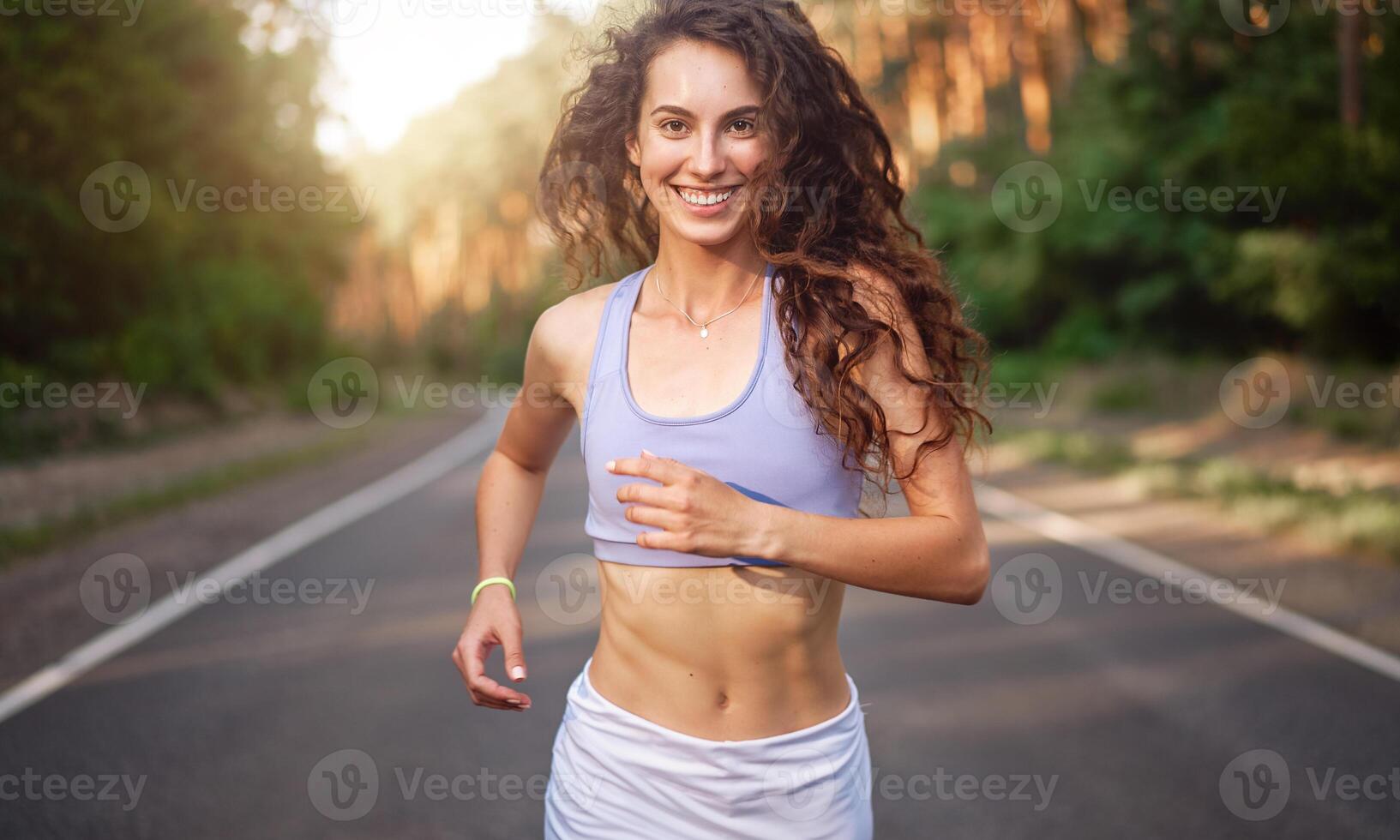 bellissimo caucasico giovane ragazza atleta corre soleggiato estate giorno su asfalto strada nel il foresta. foto