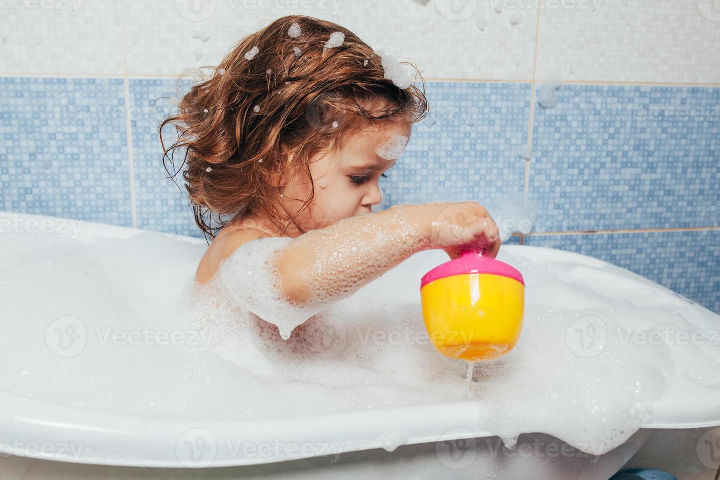 bellissimo poco ragazza assunzione un' bagno a casa. un' carino bambino è seduta nel il bagno e giocando con giocattoli e acqua. personale igiene per bambini. quotidiano igiene foto