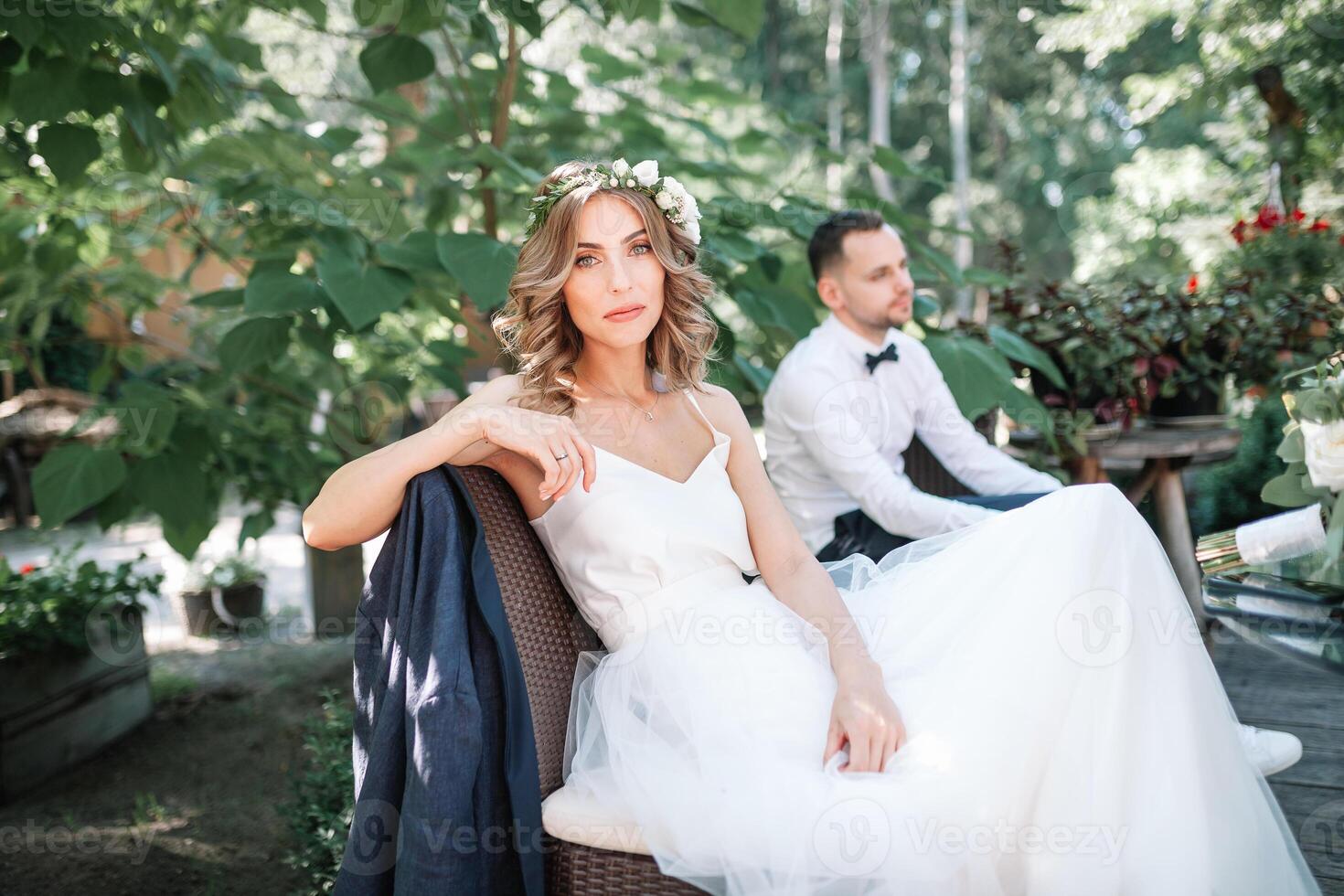 un' bellissimo sposa nel un' bianca nozze vestito e ghirlanda si siede su un' sedia Il prossimo per il sposo, riposo e preparazione per un' contento famiglia vita foto