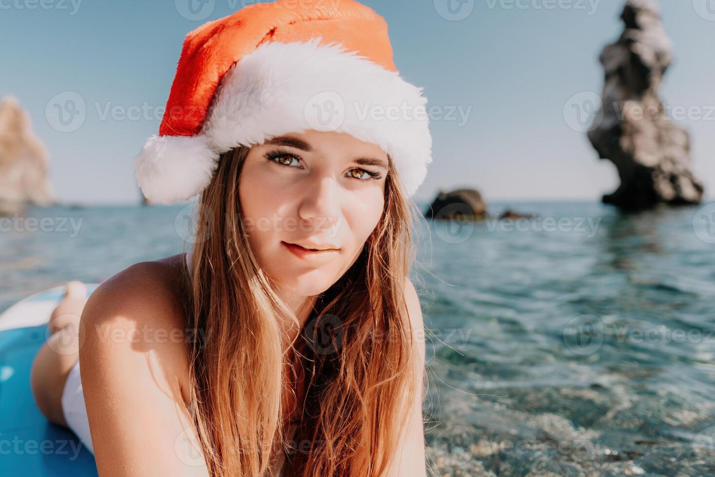 donna mare sup. vicino su ritratto di contento giovane caucasico donna con lungo capelli nel Santa cappello guardare a telecamera e sorridente. carino donna ritratto nel un' bianca bikini in posa su cenare tavola nel il mare foto