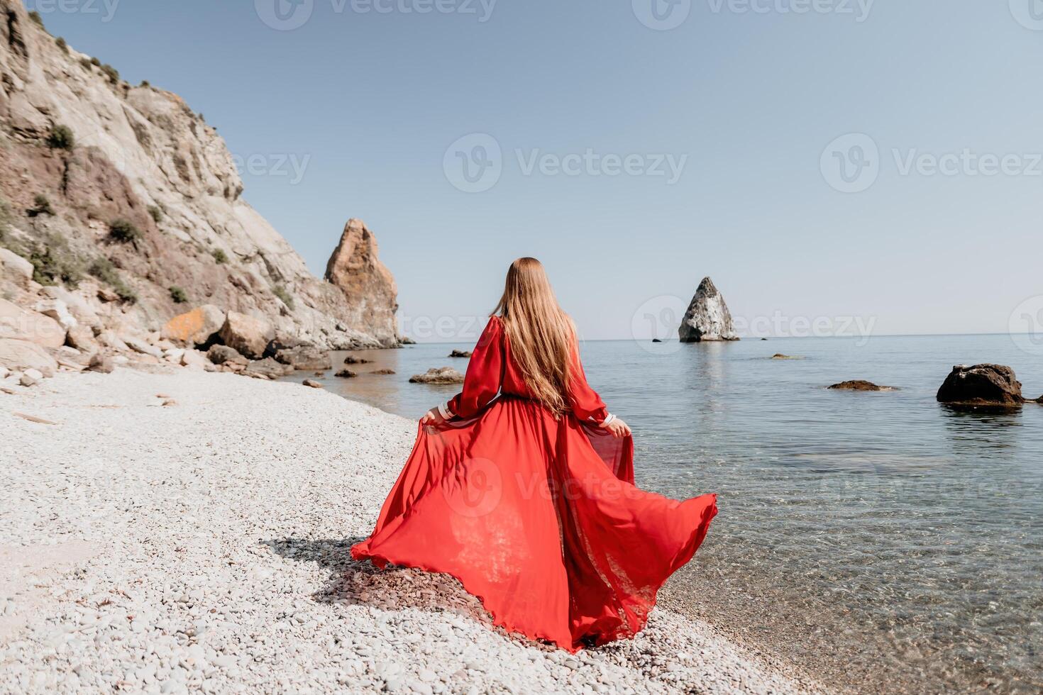 donna viaggio mare. contento turista nel rosso vestito godere assunzione immagine all'aperto per ricordi. donna viaggiatore in posa su il roccia a mare baia circondato di vulcanico montagne, condivisione viaggio avventura viaggio foto